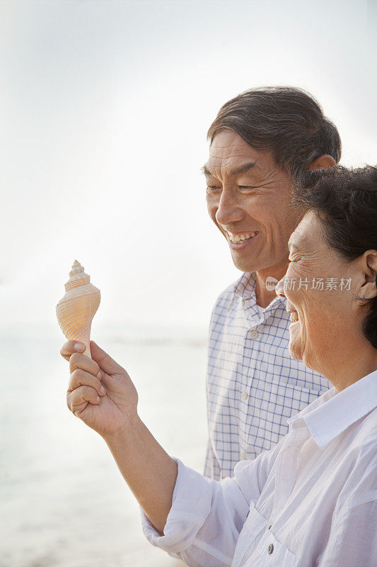 一对年老的中国夫妇在海滩上查看贝壳