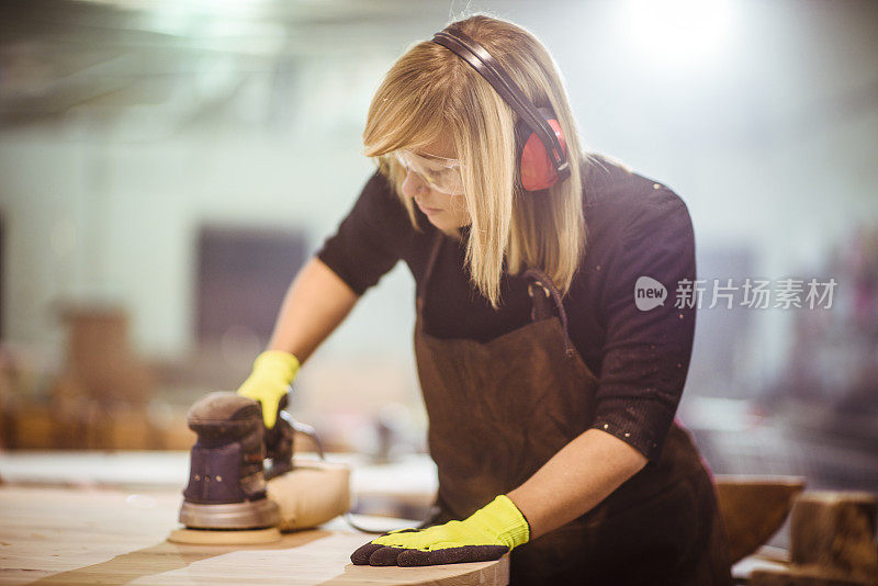 女木匠在工作台上用任意轨道的砂光机打磨木头表面