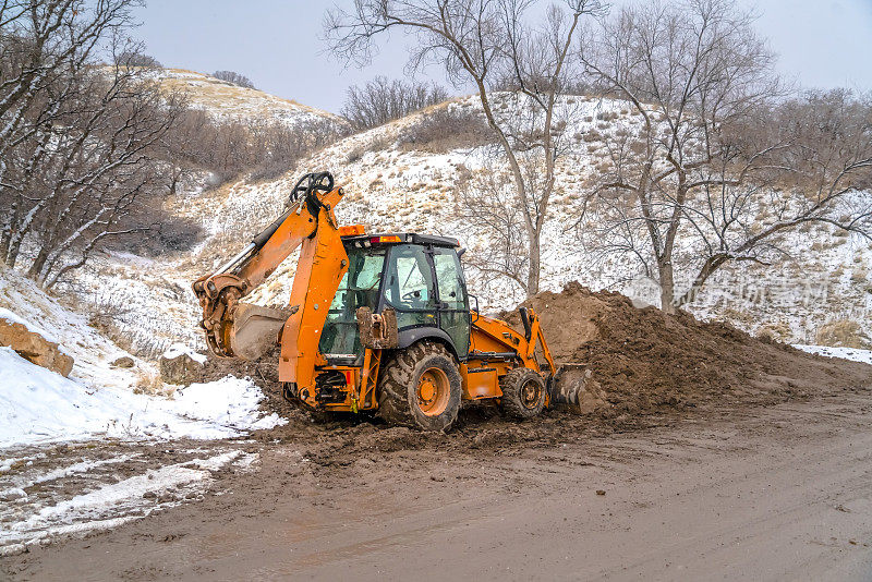 反铲装载机对抗着白雪覆盖的山丘和树木