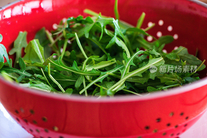 用滤锅用水冲洗新鲜的火箭叶子，特写