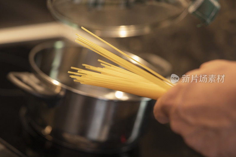 男人穿着围裙在厨房里准备食物，煮意大利面。