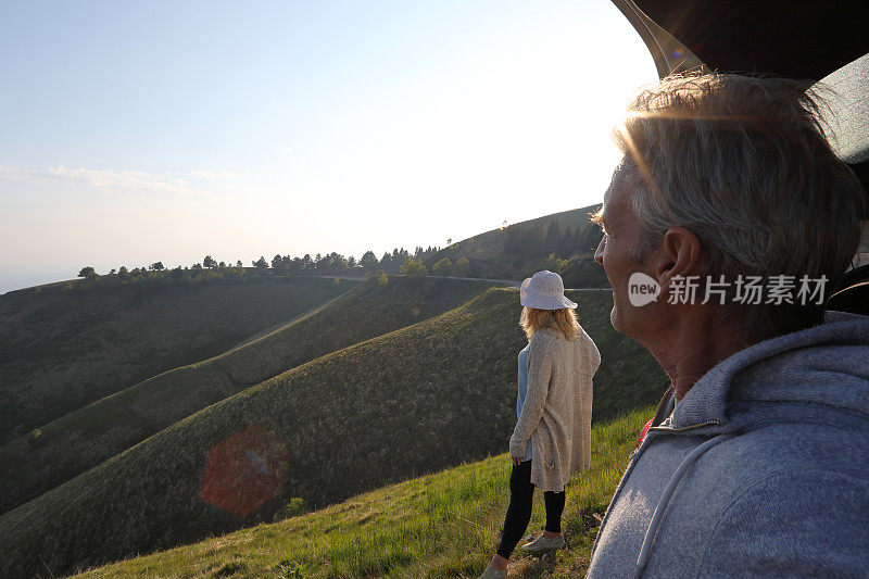 日出时，男人和女人站在草地上，旁边是汽车