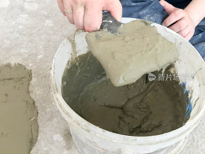 建筑工手用金属铲在一个大的白色塑料建筑桶中揉出灰泥、瓷砖胶水、水泥，用于公寓、房屋的修复、找平墙壁和浇筑