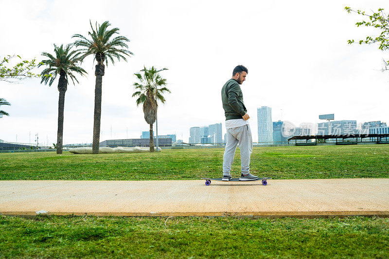 一个休闲男子在巴塞罗那公园玩长板，以城市天际线为背景