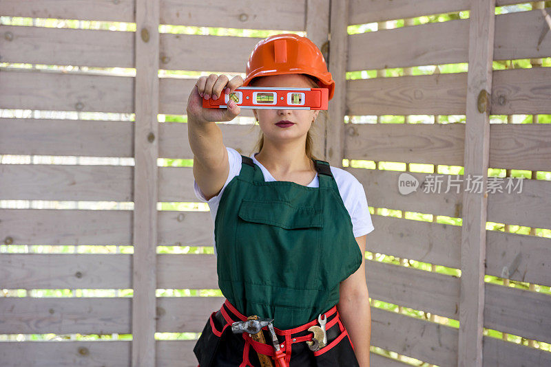 妇女与测量水平工具在建筑工地。妇女测量木墙和摆姿势的相机