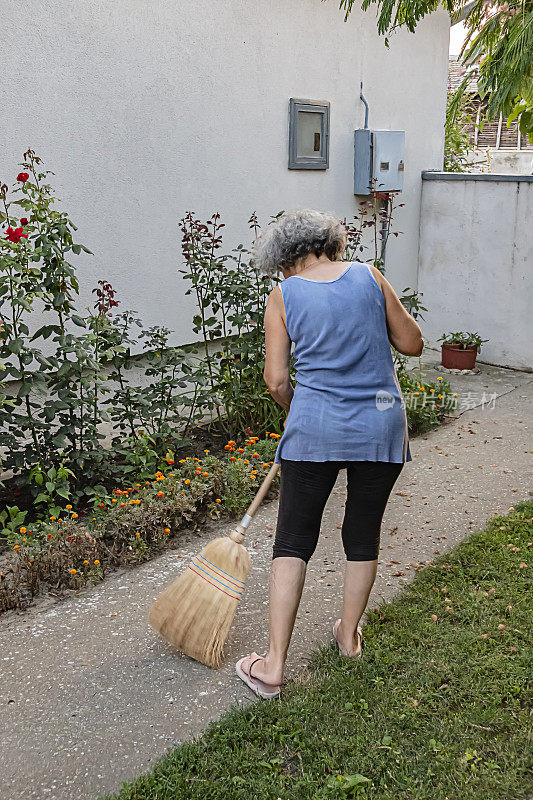 白发苍苍的老妇人正在用扫帚扫干树叶