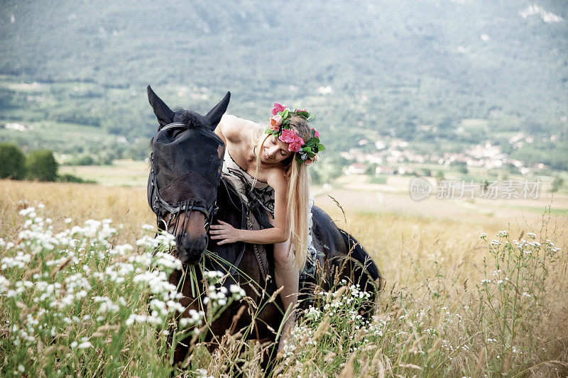 美丽的年轻女骑手在花冠拥抱她的马，而骑在野花之间-库存照片