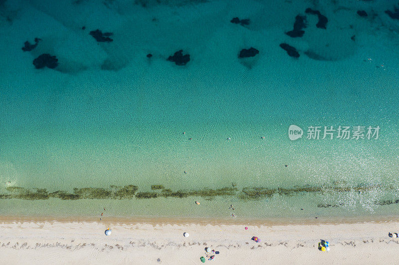 在阳光明媚的日子里，人们在透明碧蓝的海水中，鸟瞰沙滩和遮阳伞