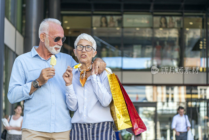 成熟的夫妇走在城市的大街上，在成功购物后吃冰淇淋