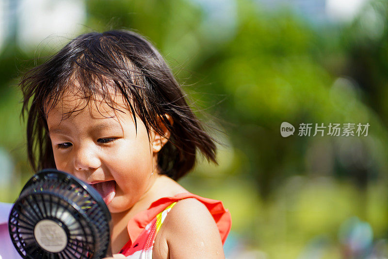 年轻的亚洲女孩试图用便携式风扇扇自己在炎热的天气。