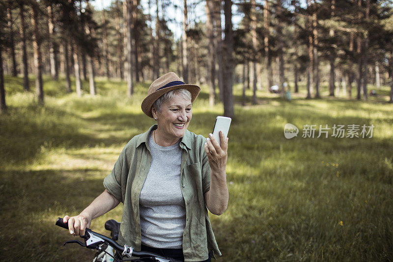 年长的女人在森林里骑自行车时用手机