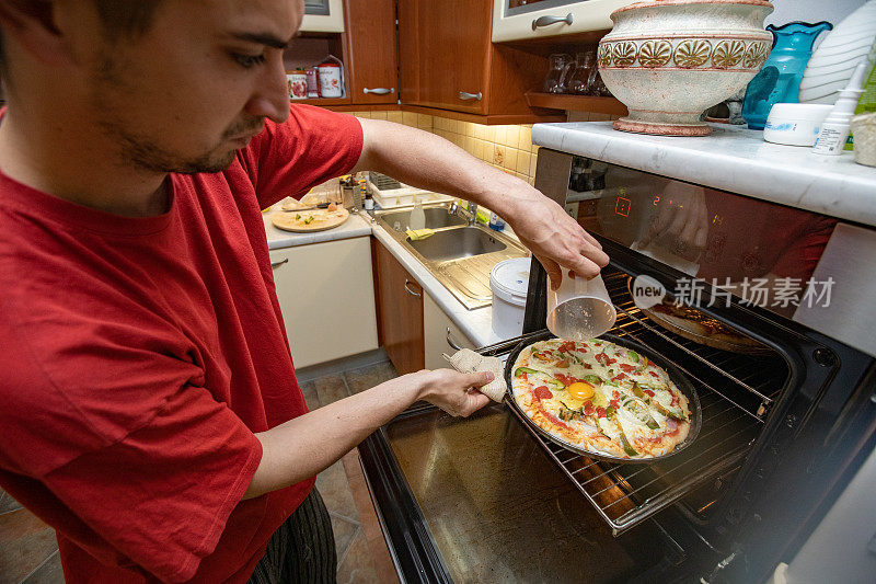 年轻的成年男子把鸡蛋倒在半烤的自制披萨上