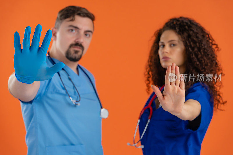 两名专业医生用听诊器看着摄像机，显示出停止标志，橙色背景