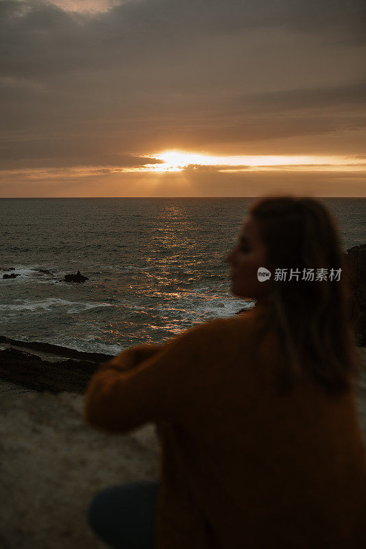 日落时坐在海边的年轻女子