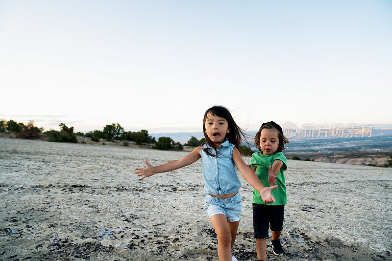 小弟弟和小妹妹，四岁和两岁，在科罗拉多西部Fruita附近的一块大石头上跑步，在夕阳下徒步旅行