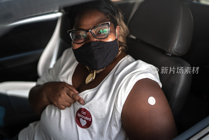 一个快乐的女人在车里的肖像，戴着“接种疫苗”贴纸的面具