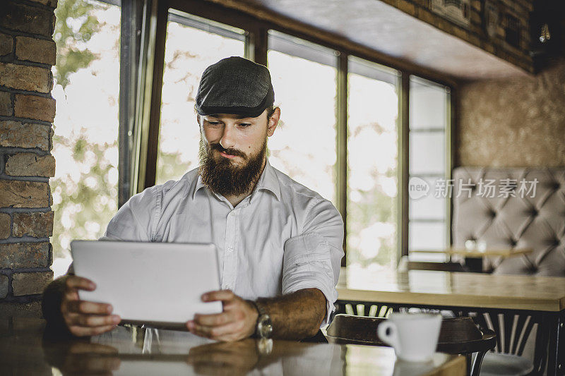 在咖啡店里使用数码平板电脑――一个年轻的商人正坐在咖啡厅里，利用他的咖啡休息时间上网