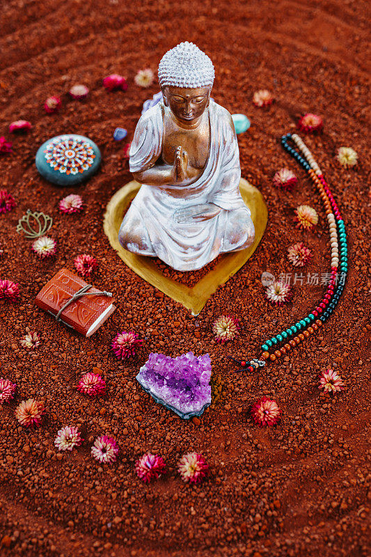 一个神圣的冥想仪式的近距离静物在红棕色的土壤上与一个白色的金色佛陀，紫水晶，念珠和各种精神对象