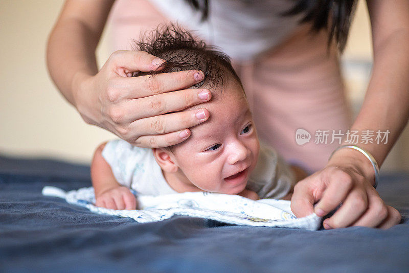 妈妈在帮助刚出生的小男孩的同时，练习抬起和托起他的头，躺在他的肚子上