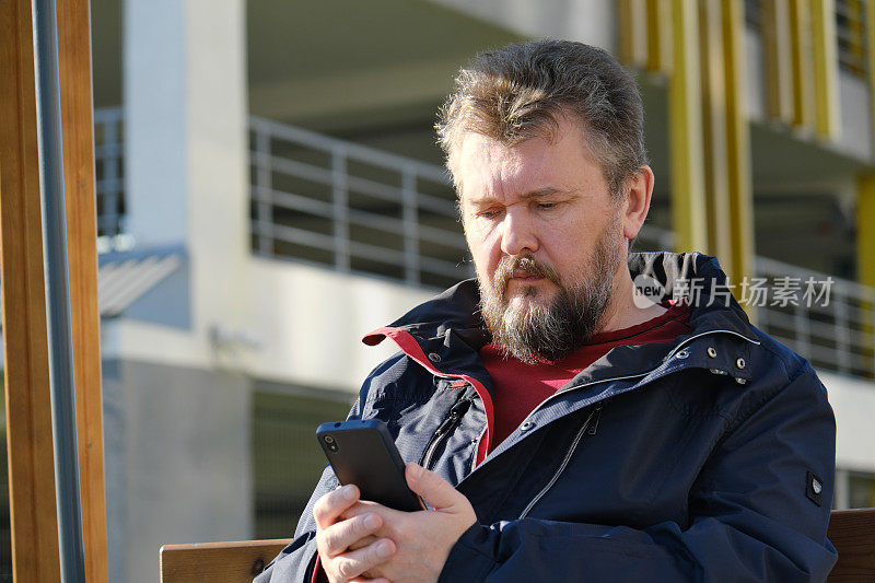 一个成熟的男人坐在长凳上用手机