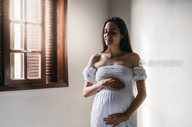 在卧室里闭着眼睛，双手放在肚子上的孕妇的肖像