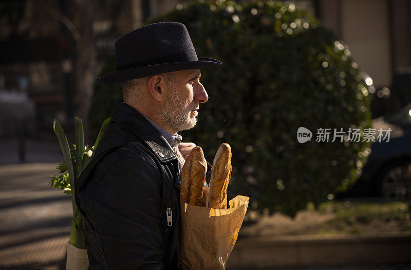 一个戴着帽子的成年人在街上拿着面包和蔬菜袋。马德里,西班牙