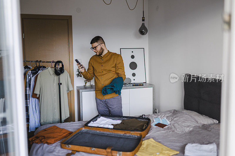 英俊的男人在酒店预订，准备旅行假期整齐地打包行李的衣服和配件