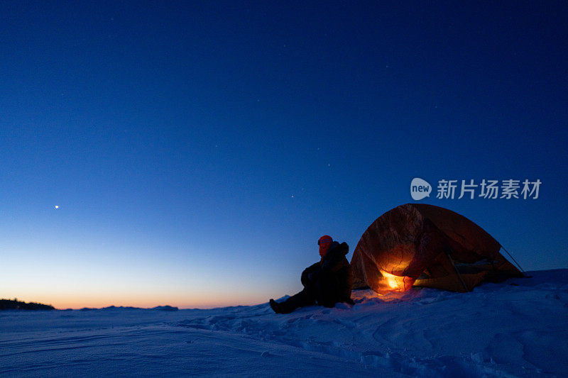 男子望向冰雪覆盖的雪地，背景是露营的帐篷