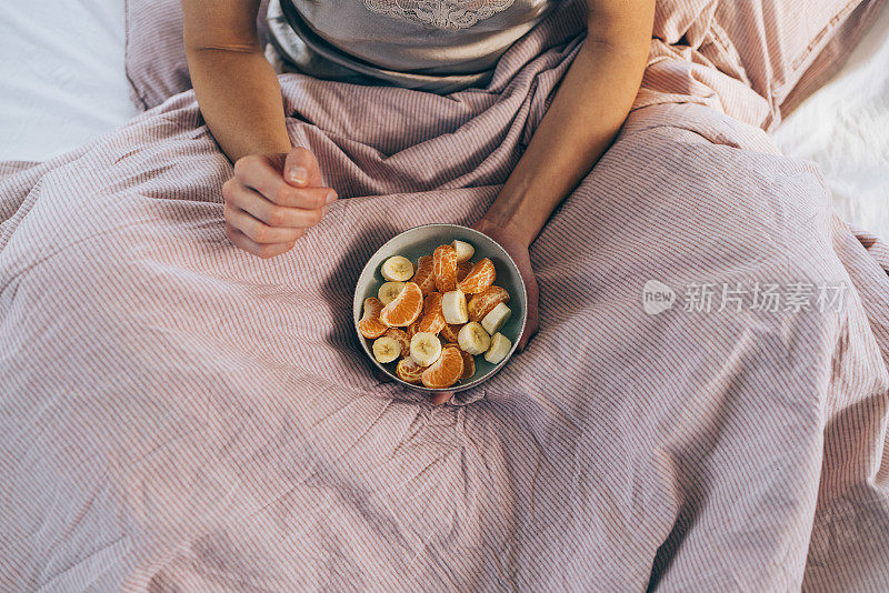 床上早餐:一个穿着睡衣拿着一碗水果的认不出来的女人