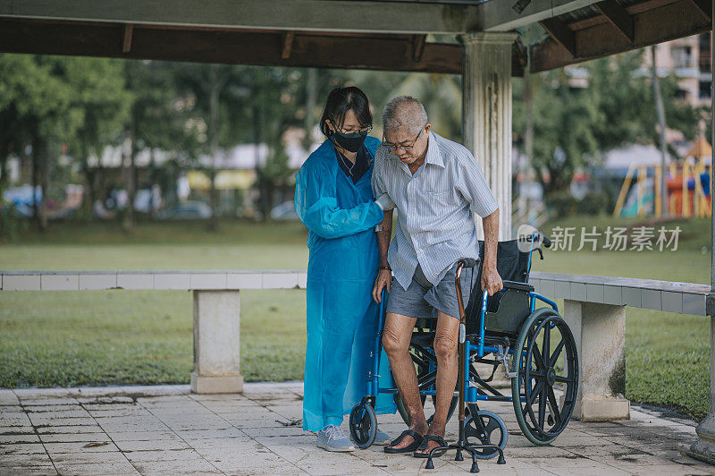 亚裔中国女理疗师帮助老年男子从轮椅上站起来，拄着拐杖在公园里散步