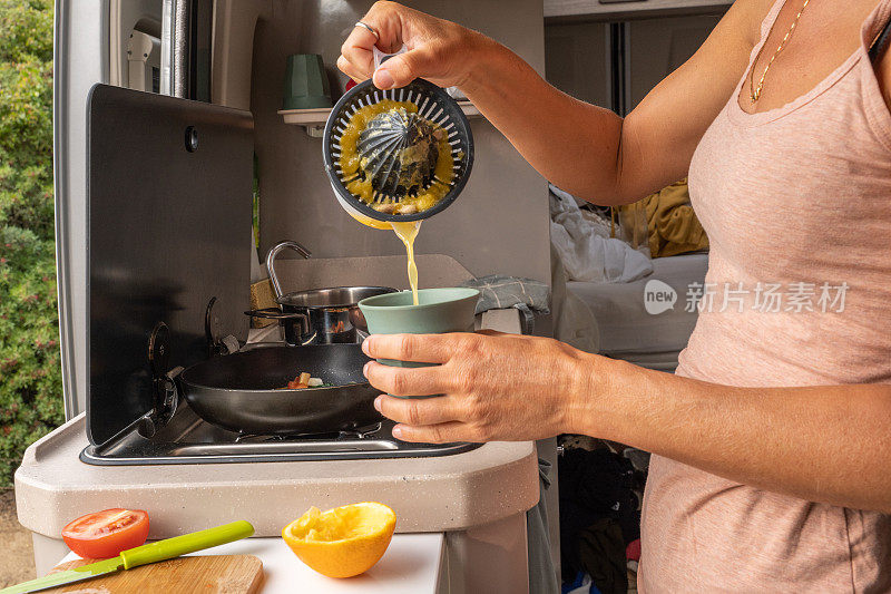 年轻女子在她的露营车里做新鲜的橙汁，以健康的食物开始一天的生活，面包车的生活理念