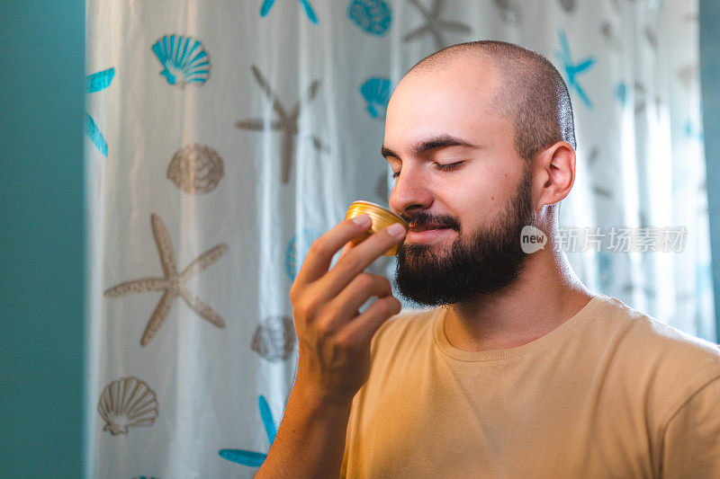 一个秃顶的年轻人在浴室镜子前闻胡子膏的特写