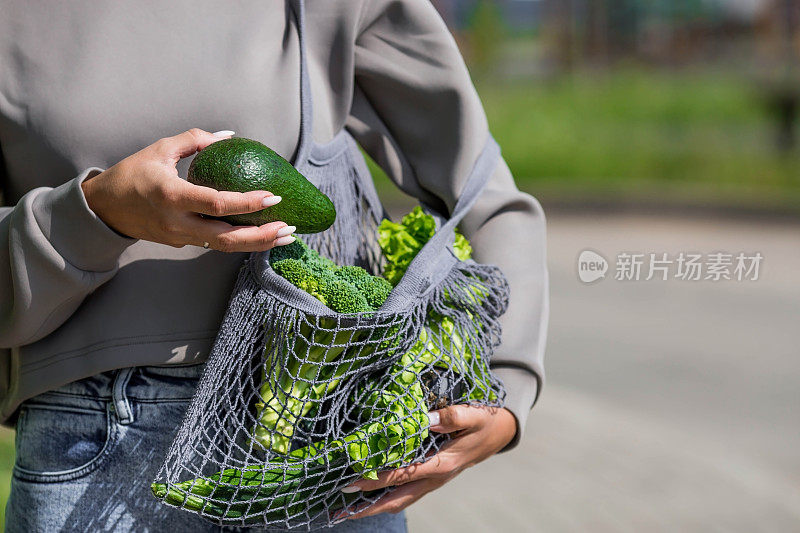 女性用手串线包和青菜特写。一个买食物的女孩。健康营养、素食和生态的概念。拒绝使用塑料袋。