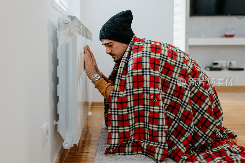 可怜的男人盖着毯子摸着暖气片