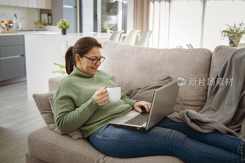 女人躺在沙发上用笔记本电脑喝咖啡