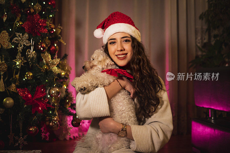 一个白人女孩抱着一只狗在圣诞树旁