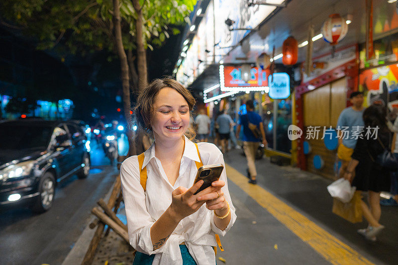 一个拿着智能手机的女人晚上走在城市里