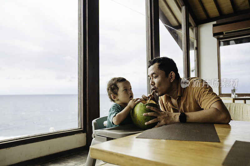 亚洲男人和他的儿子坐在桌子上喝椰子水