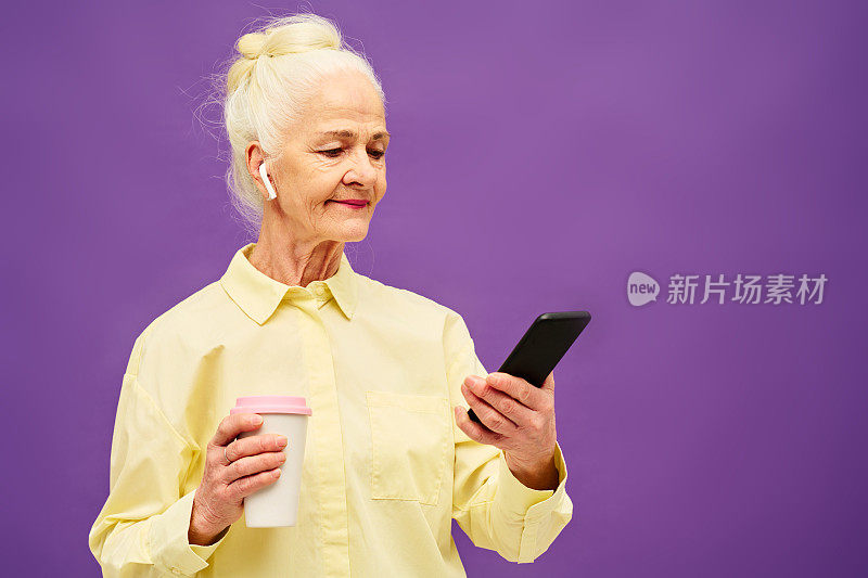 老年妇女拿着一杯咖啡在手机上看在线视频
