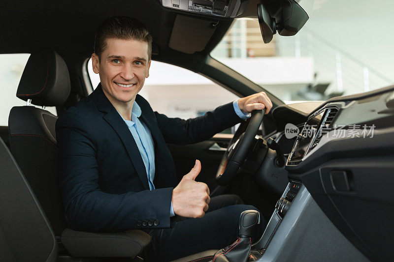 快乐的年轻汽车销售员坐在新车里，竖起大拇指，推荐现代经销商