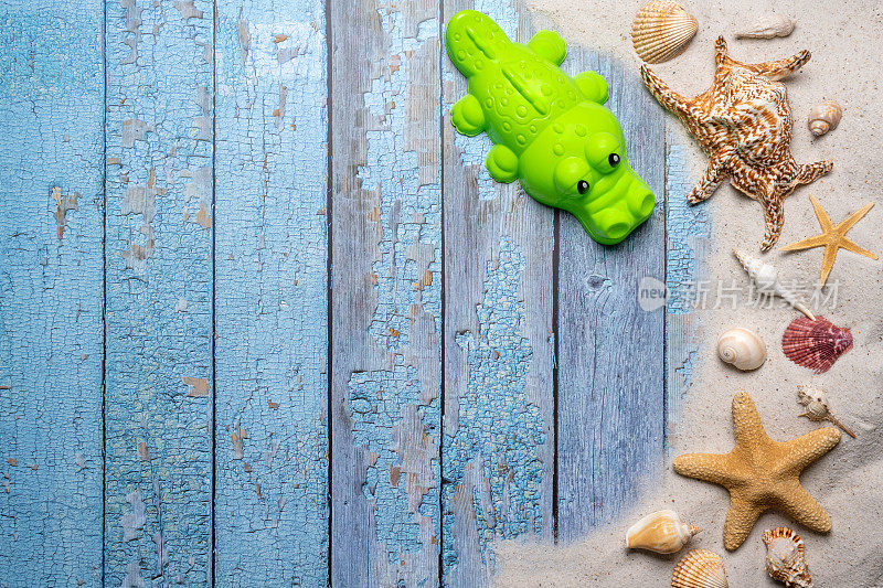 夏天，海滩和度假的概念与自由文本空间。前视图。平面布局，绿色的沙子形式的鳄鱼，大海星和海贝壳和各种海贝壳和细沙滩砂在一个古老的蓝色木板背景