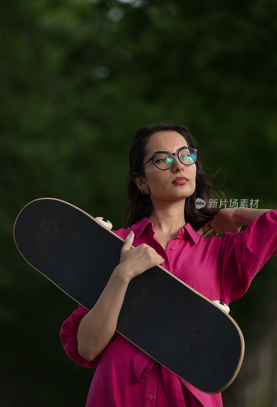 穿着粉红色裙子的漂亮年轻女子正拿着滑板。