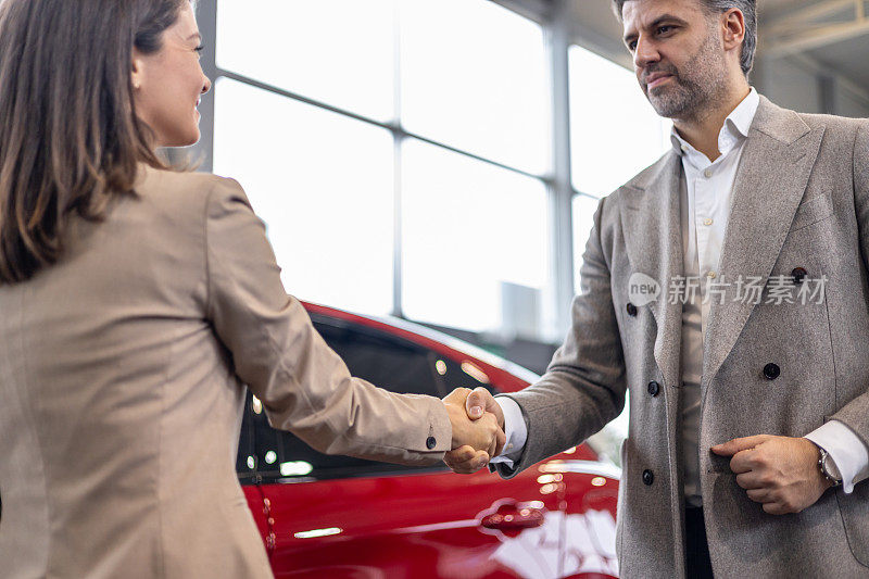 一男一女在汽车经销店红车前握手
