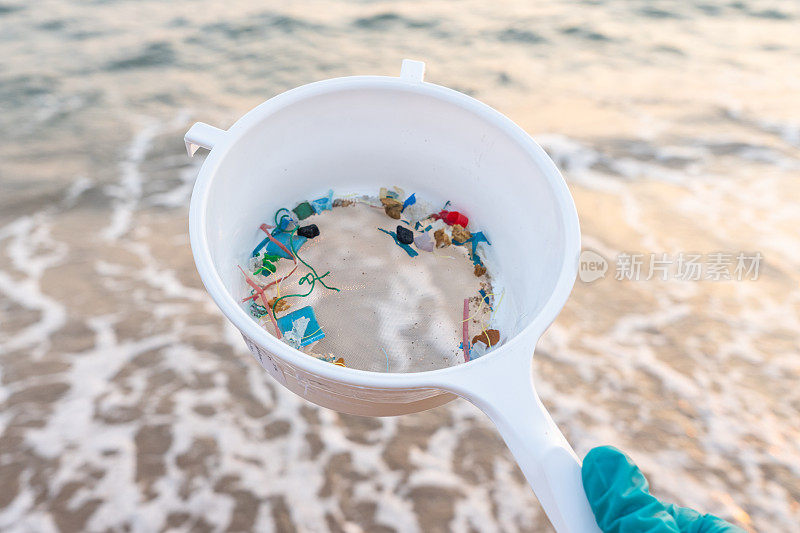 关注手头，年轻女子一边做海滩清洁志愿者，一边用滤器从海水中筛选微塑料——环境问题、污染和生态系统预警概念