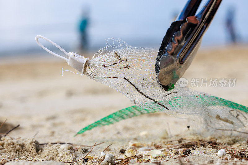 一名志愿者用钳子清理海滩上的塑料碎片和垃圾的特写