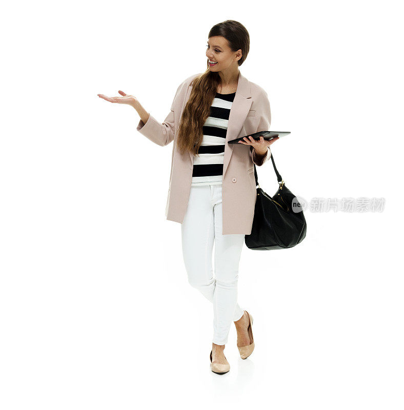 白种人年轻女主持人穿着外套，手拿钱包，手持平板电脑，站在白色背景前