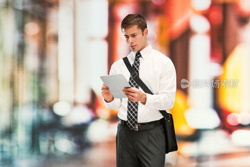 背景模糊的白人男性商务人士在户外戴着信使包，拿着包，使用触摸屏