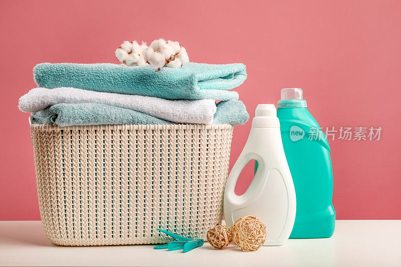 以粉红色为背景，装有毛巾、棉条、洗涤剂、竹球及衣夹的洗衣篮