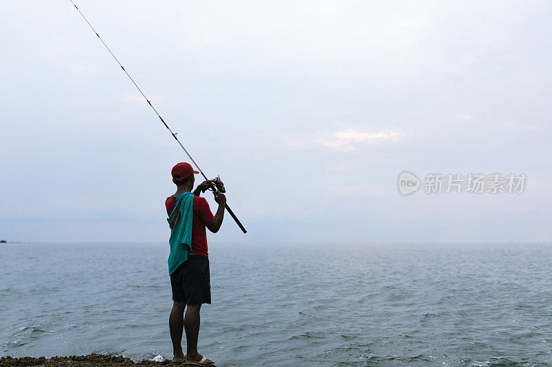 亚洲男子戴着帽子在海滩上钓鱼