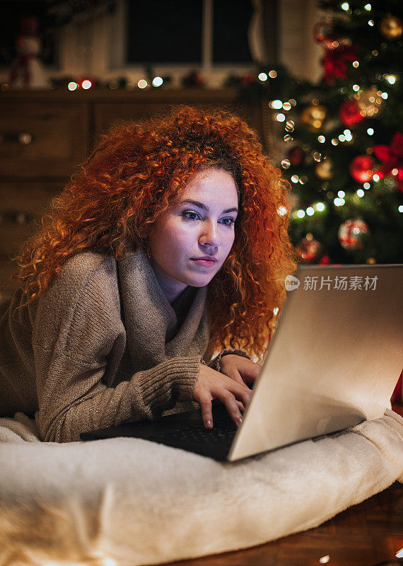 年轻美丽的女孩享受在家里使用笔记本电脑在一个舒适的圣诞气氛